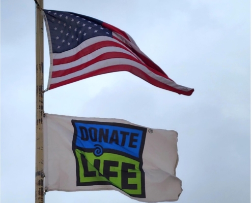 Photo of the American flag and Donate Life flag waving on a flag pole.