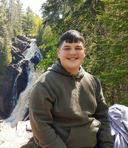Photo image of Ryan Stoway in a hoodie with a waterfall and wooded scenery in the background.