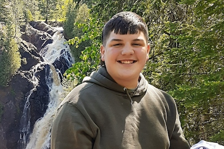 Photo image of Ryan Stoway in a hoodie with a waterfall and wooded scenery in the background.