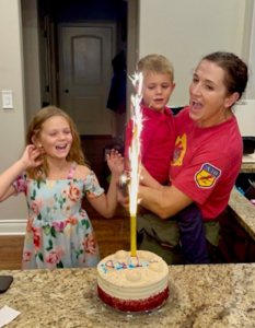 A mother and two children gather around a cake with a sparkling candle.