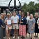 A group of men and women posed in front of a tall sculpture that represents the gift of life through organ donation.